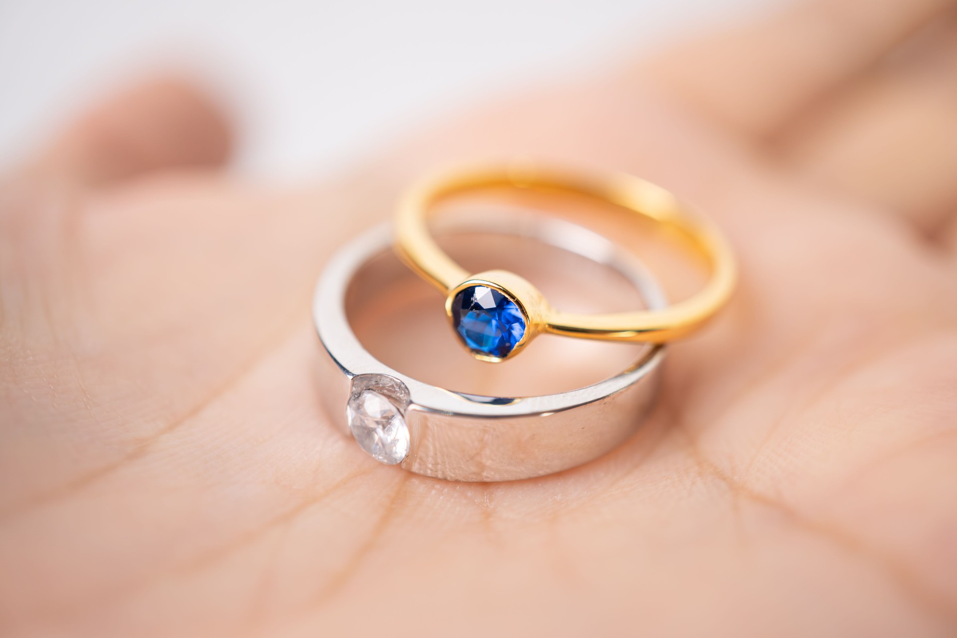 Stacked gold and silver rings set with diamonds and blue sapphires laid on hand palm background. Detail macro photography.